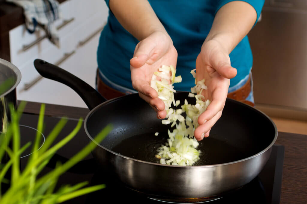 Person gibt Zwiebeln in eine Bratpfanne