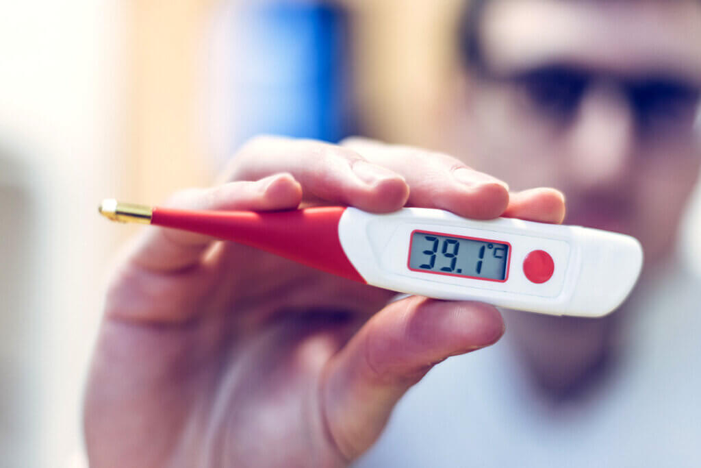 Mann hält rot-weißes Fieberthermometer in der Hand