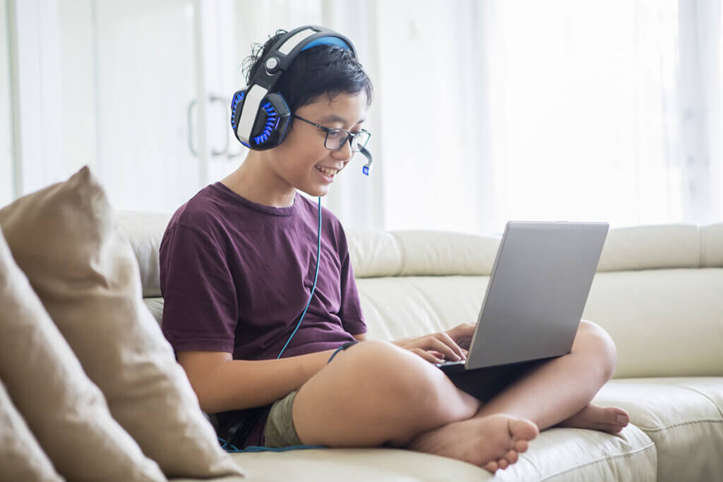 Junge mit Laptop und Headset auf Sofa