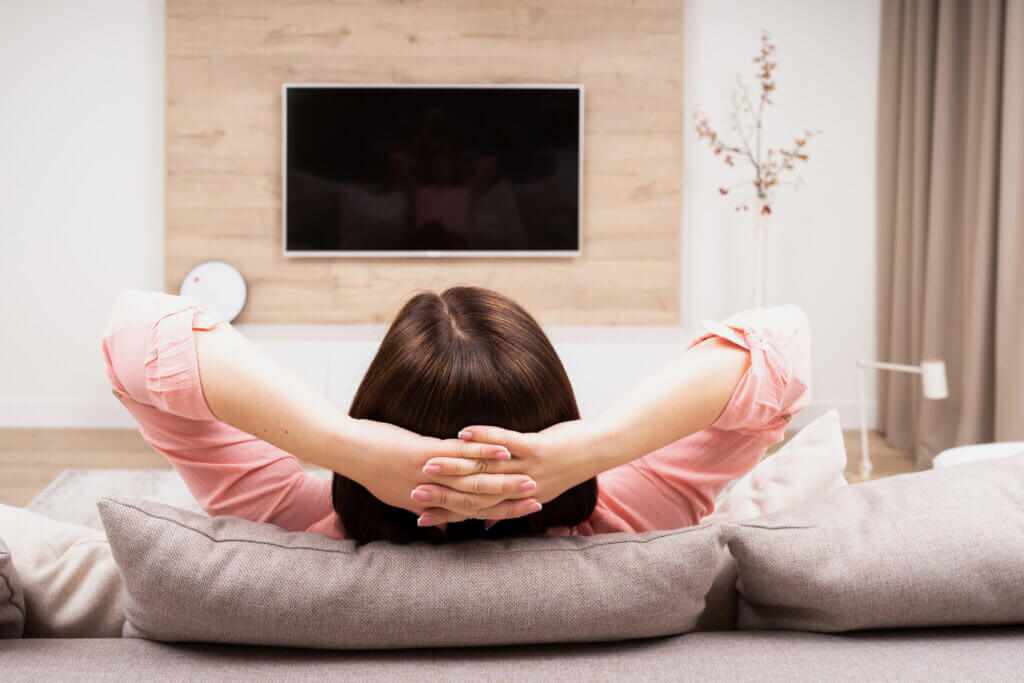 frau mit verschraenkten haenden sitzt auf sofa vor dem fernseher