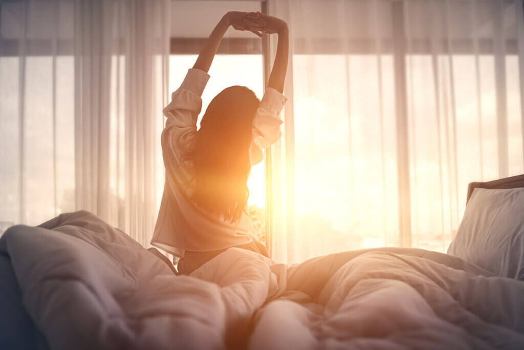 Frau streckt sich im Sonnenbett sitzend im Bett