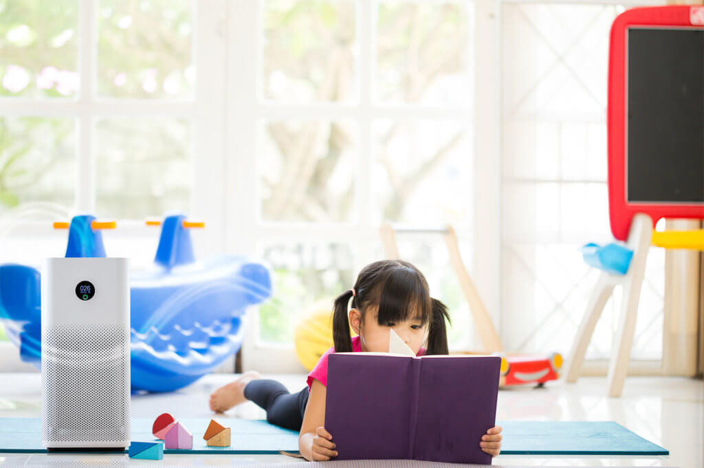 Kleines Kind liegt auf dem Boden und liest in einem Buch - daneben steht ein Luftreiniger