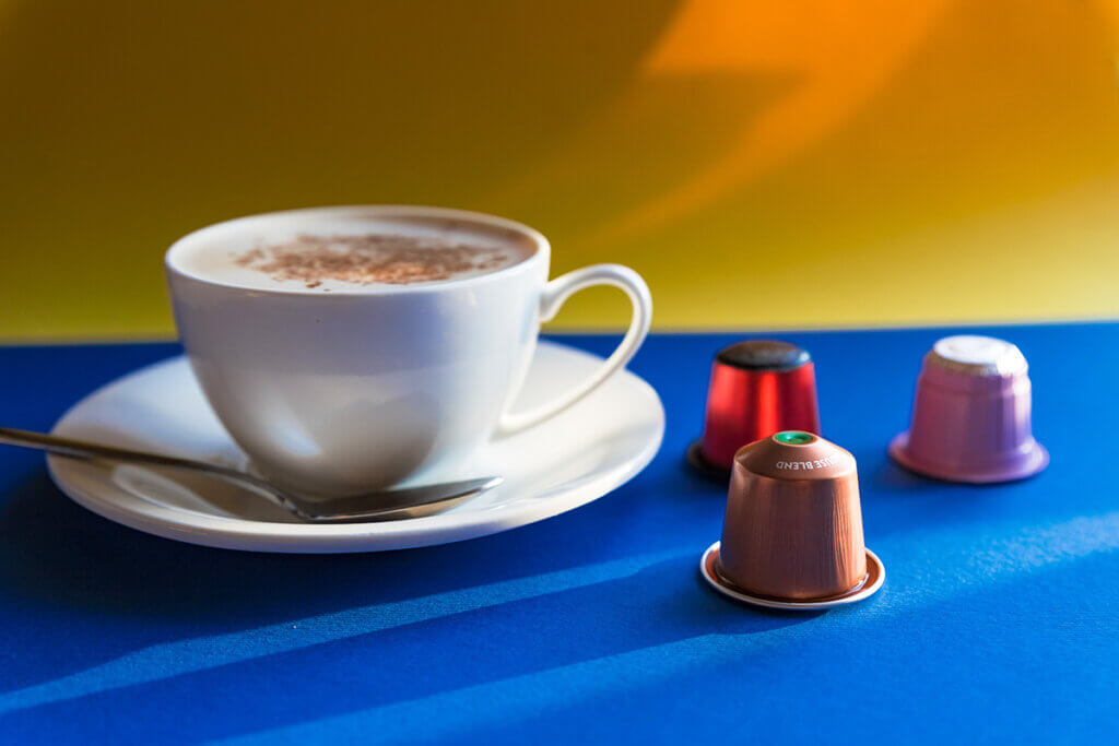 Ein Kaffeegetränk in einer Tasse neben Nespresso-Kapseln