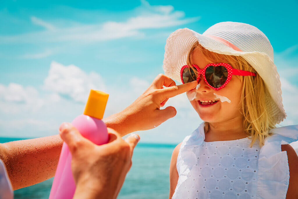 Elternteil cremt Gesicht eines Kindes mit Sonnencreme ein