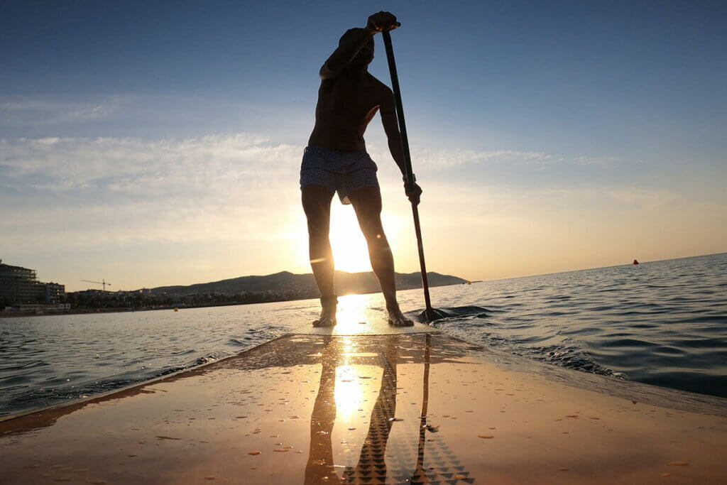 Person steht auf SUP-Board bei Sonnenaufgang